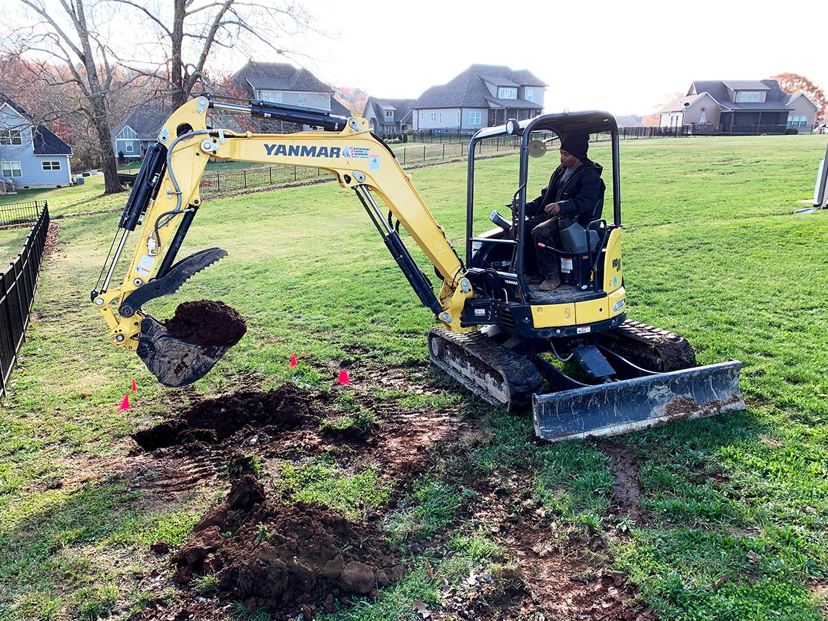 Excavator digging hole into lawn