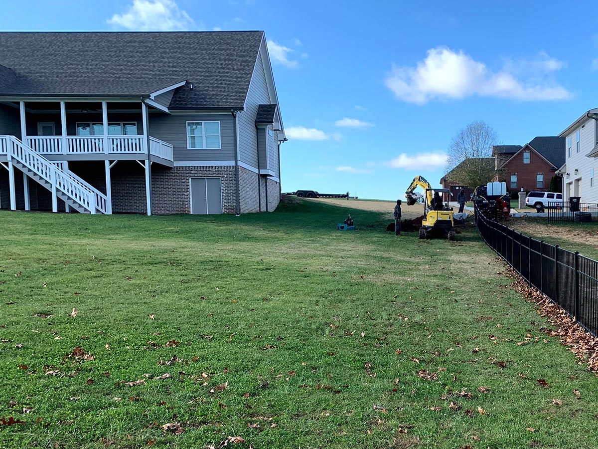 Lawn with workers and excavator on it