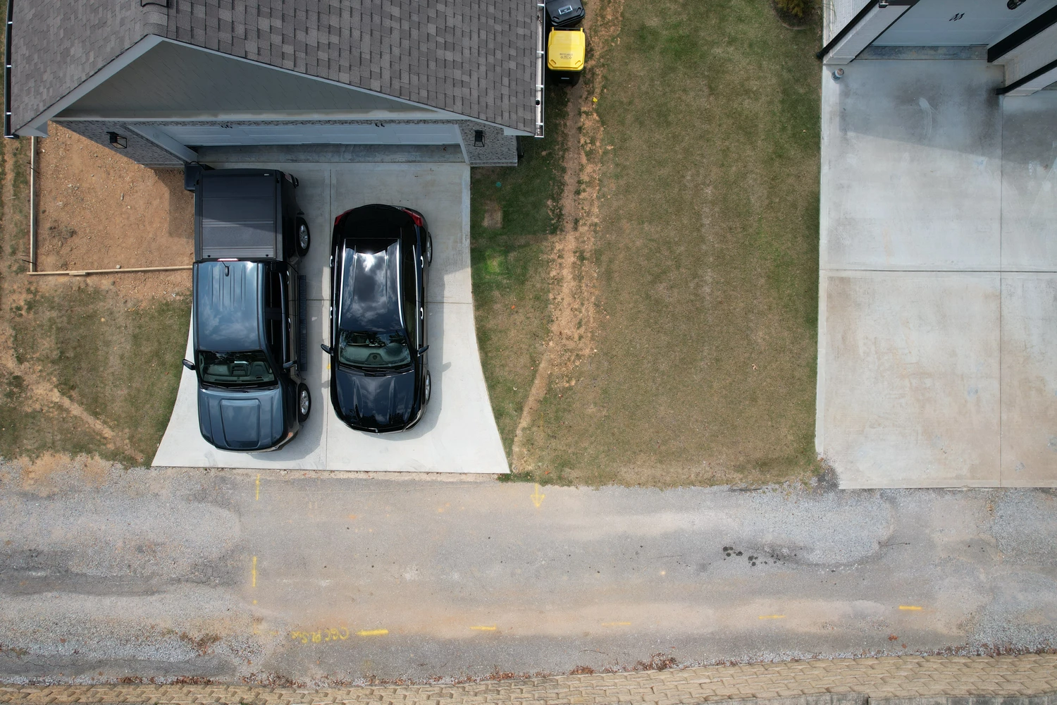Clean concrete driveway frames two parked cars beside a narrow stretch of sun-browned lawn ready for landscape refresh
