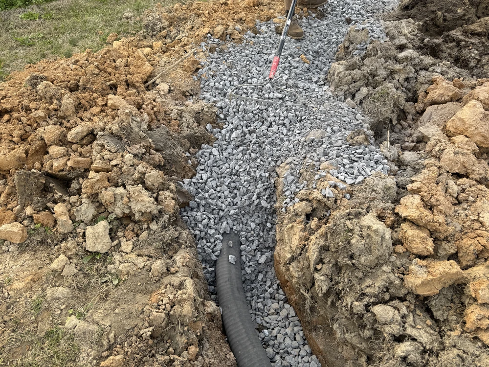 Gravel filled French drain trench with exposed soil and black pipe during yard drainage work in Collegedale TN.