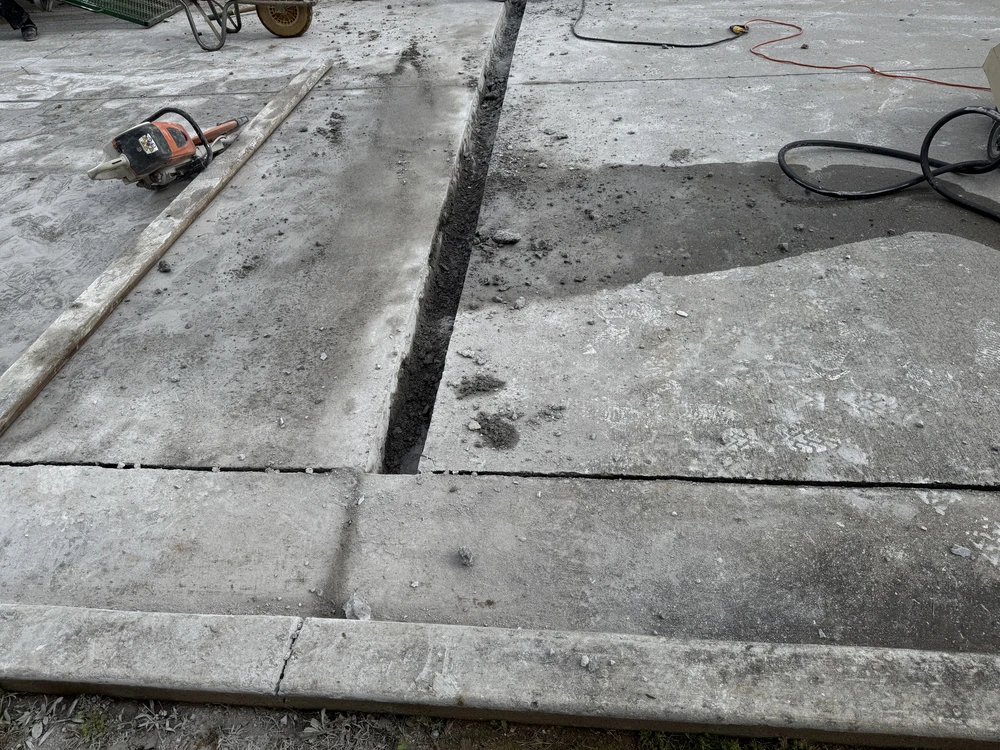 Cut concrete drainage channel across a weathered driveway with tools and hoses at a Collegedale TN property.