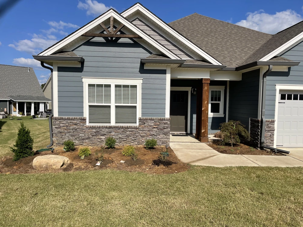 Fresh foundation landscaping softens the blue-gray home with dark mulch, young shrubs, stone accents, and a tidy lawn