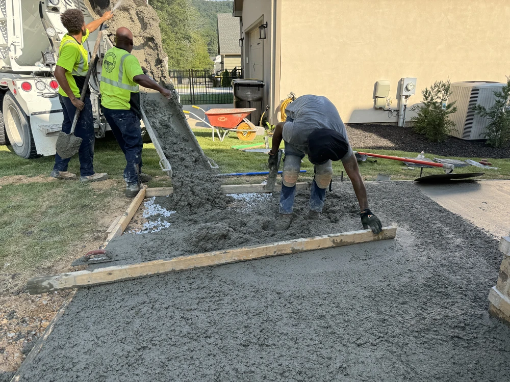 Concrete crew pours and levels a new patio slab beside a home with wet concrete truck chute in Apison TN.