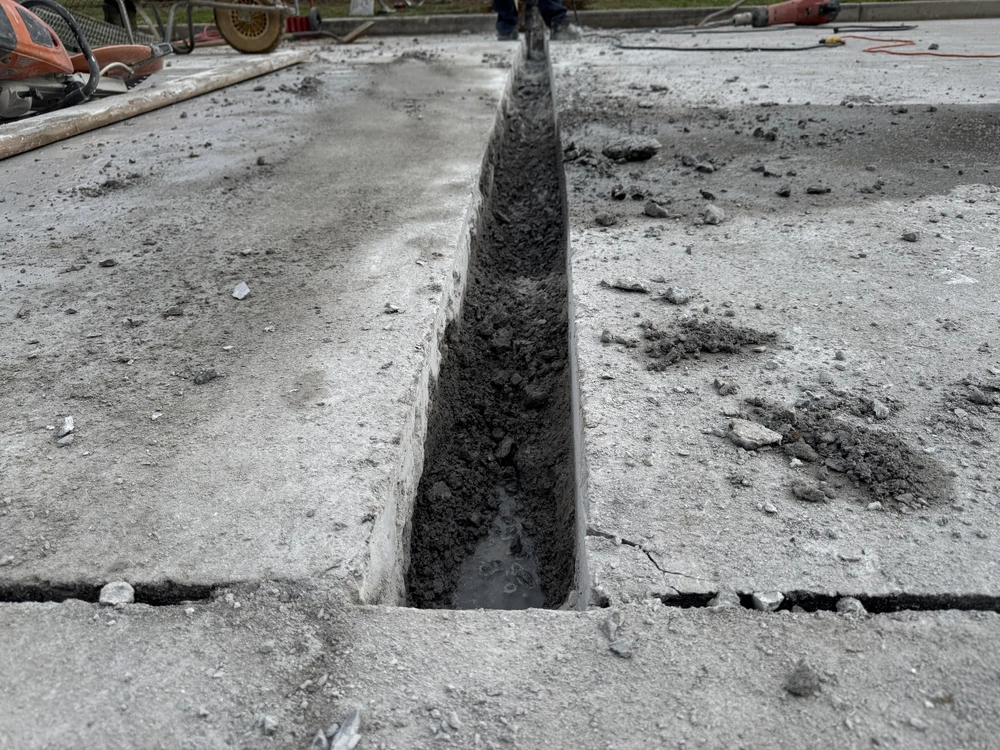 A narrow trench cuts through wet concrete, showing fresh drainage work being shaped into the hard surface