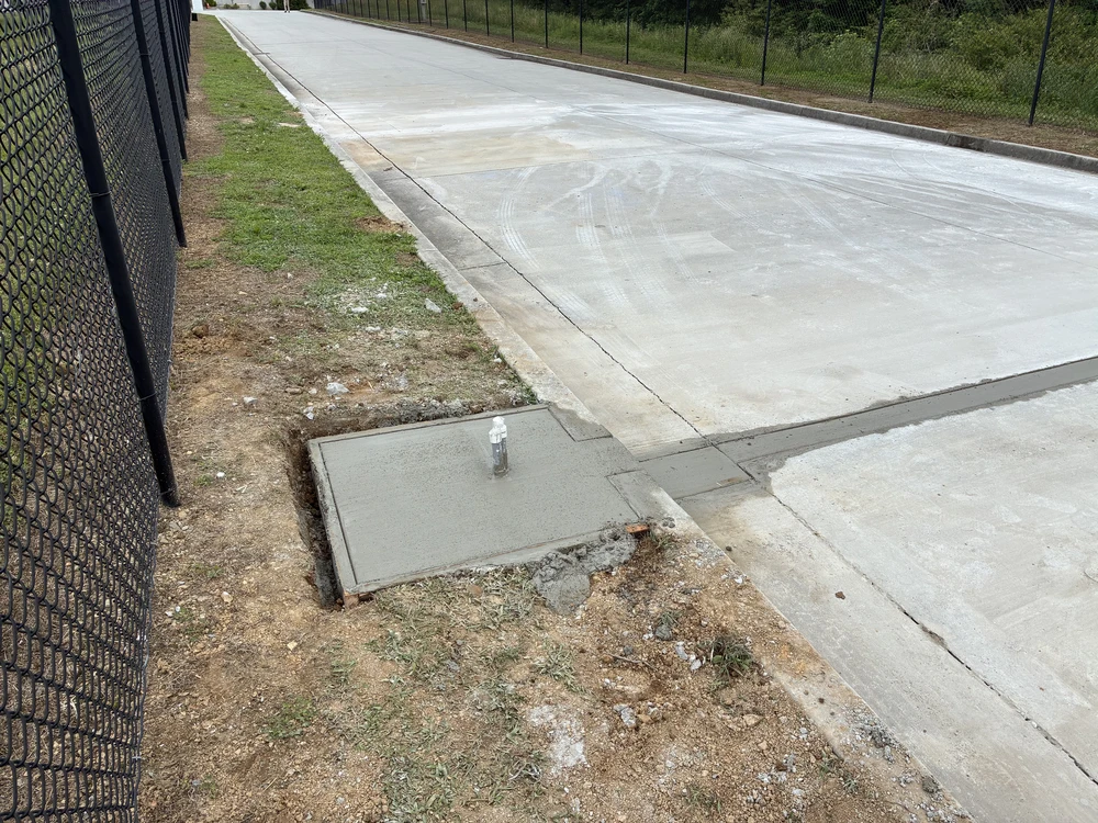 Chattanooga, TN concrete drive shines bright beside a black fence, with a small curb drain carrying water from the smooth slab