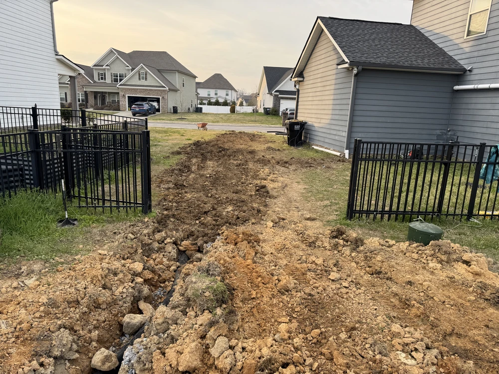 Hixson, TN backyard shows fresh trench work cutting through clay soil between black gates for a cleaner drainage path