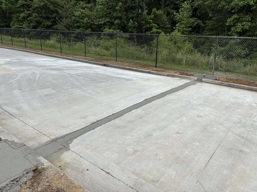 Hixson, TN concrete drive gleams beside a black fence, with a clean drain line guiding runoff toward the wooded edge