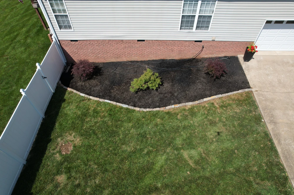 Ooltewah, TN front bed curves with fresh black mulch, soft shrubs, and clean stone edging against a brick home