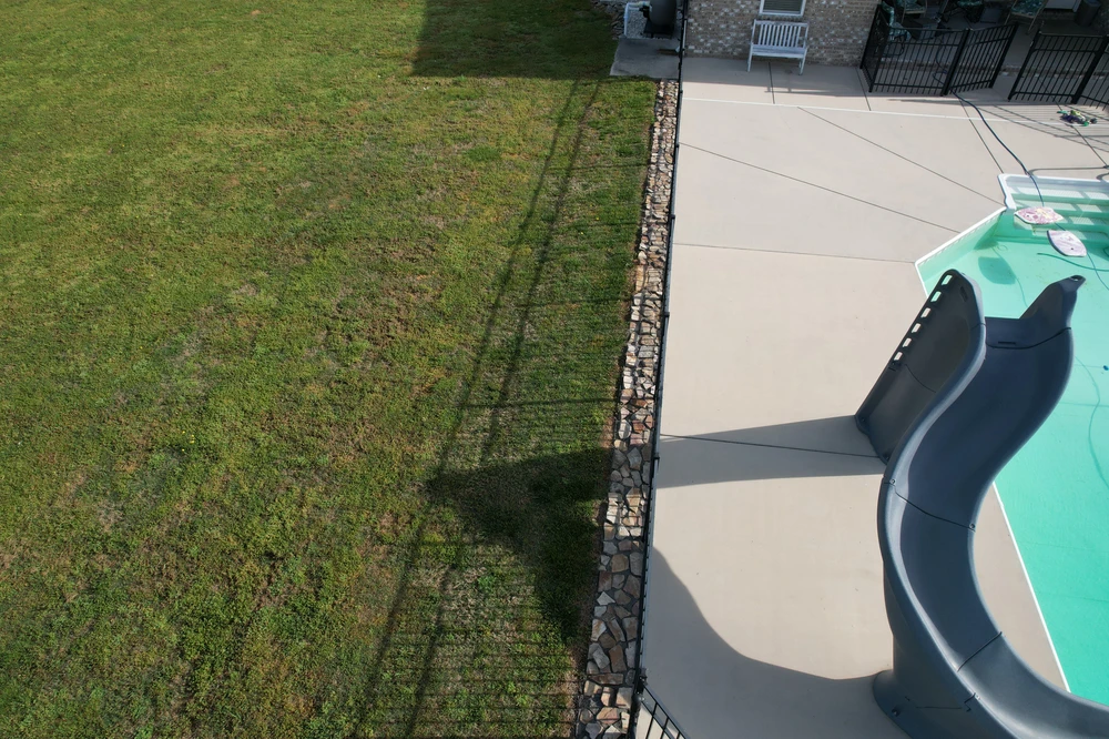 Stamped concrete pool edge runs beside a narrow river rock border, creating a crisp transition from lawn to smooth deck