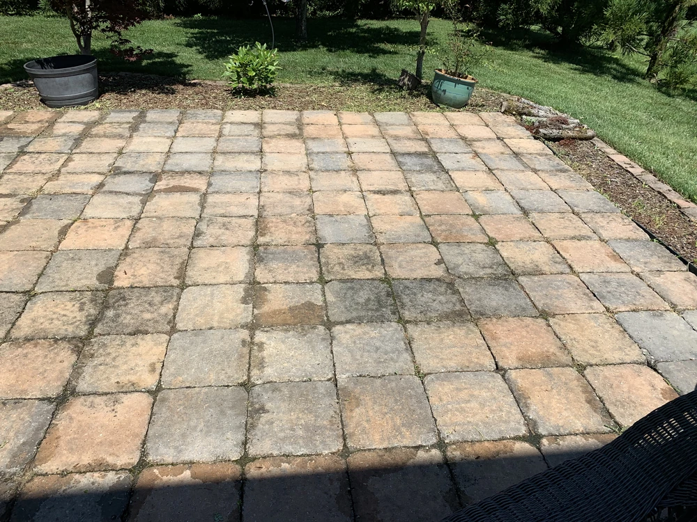 Weathered stone paver patio bordered by garden beds and green lawn in a shaded backyard.