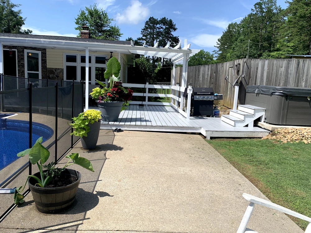 White hardscaping deck with pergola black grill gray hot tub tall planters pool fence and wood privacy fence.