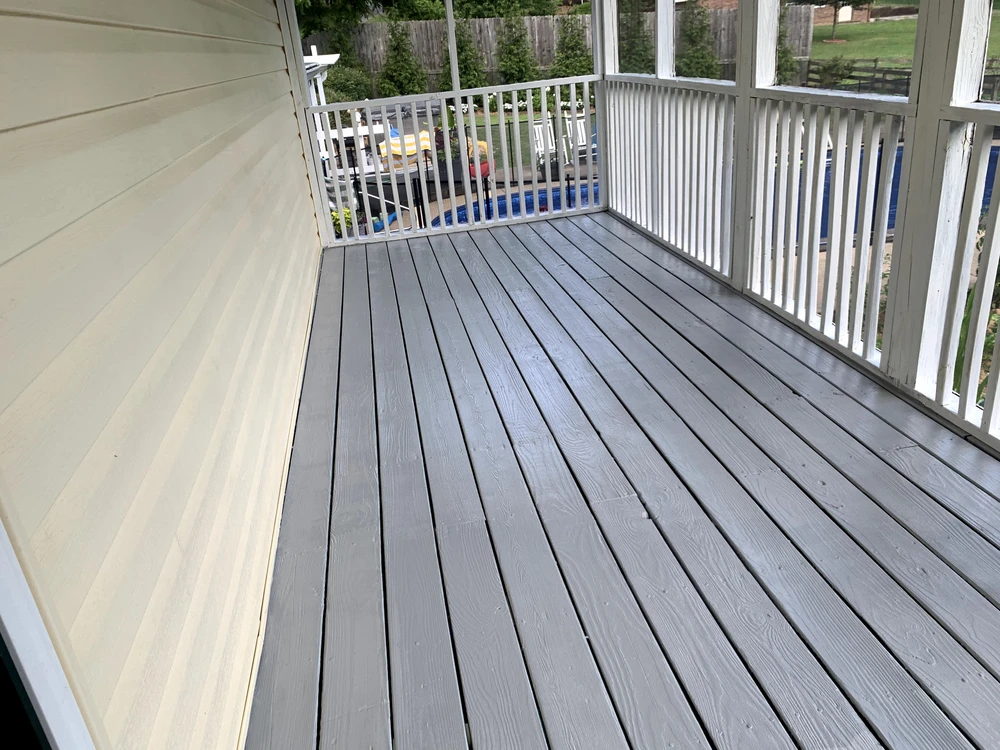 Screened porch with gray deck boards white railings beige siding and a pool visible through the balcony.