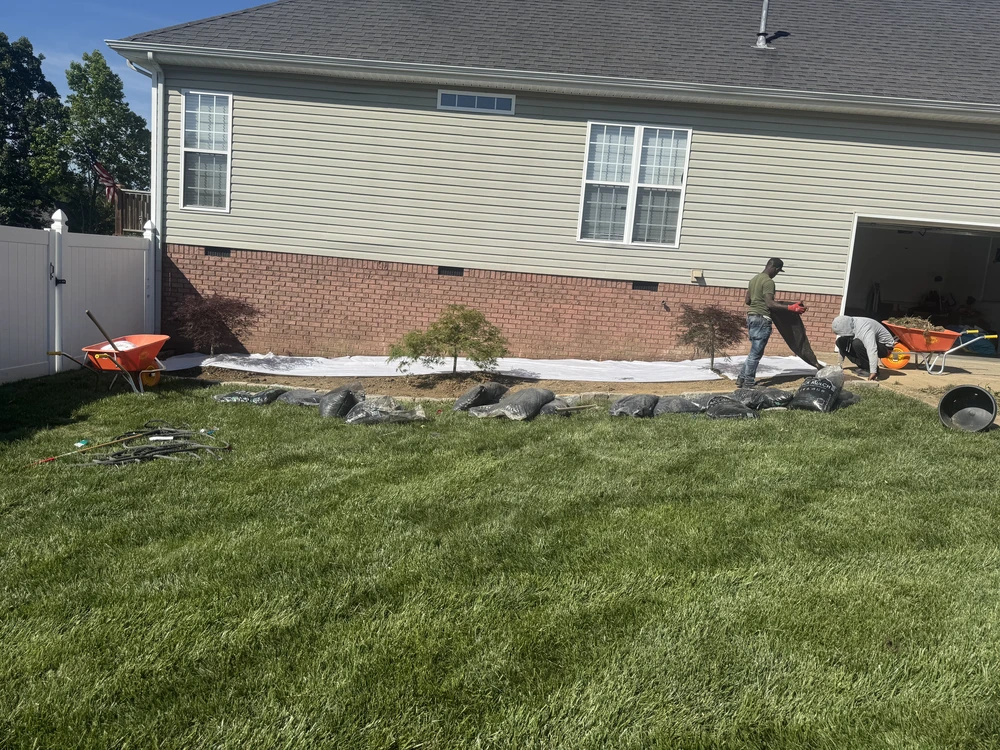 Backyard landscaping work beside a brick and siding home in Soddy Daisy TN with soil fabric and tools on the lawn.