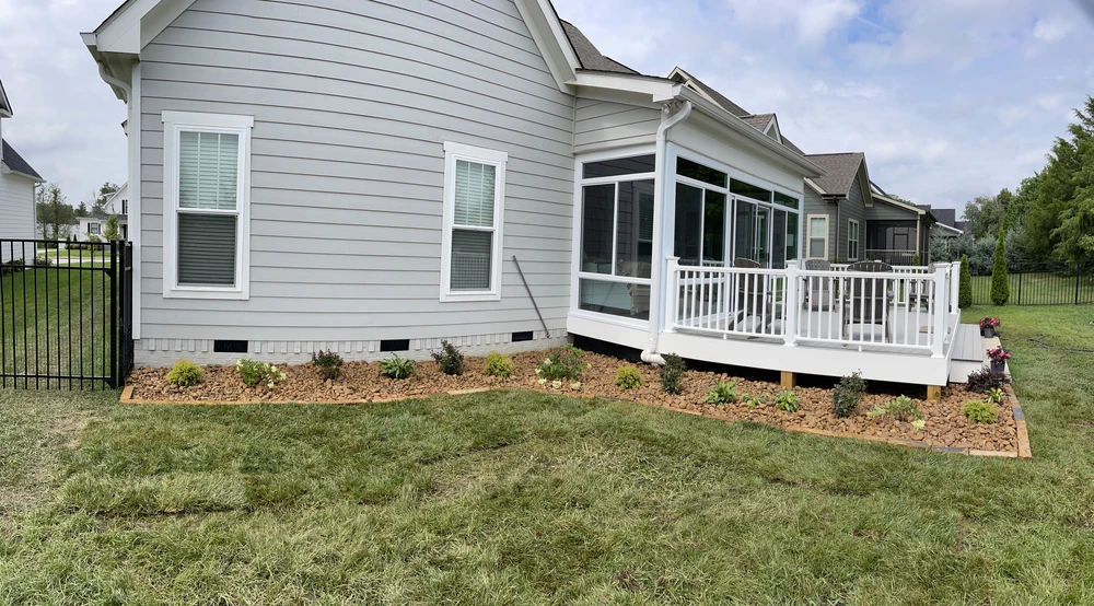 New mulched garden bed with small shrubs wraps around a gray house and white deck in Red Bank TN.
