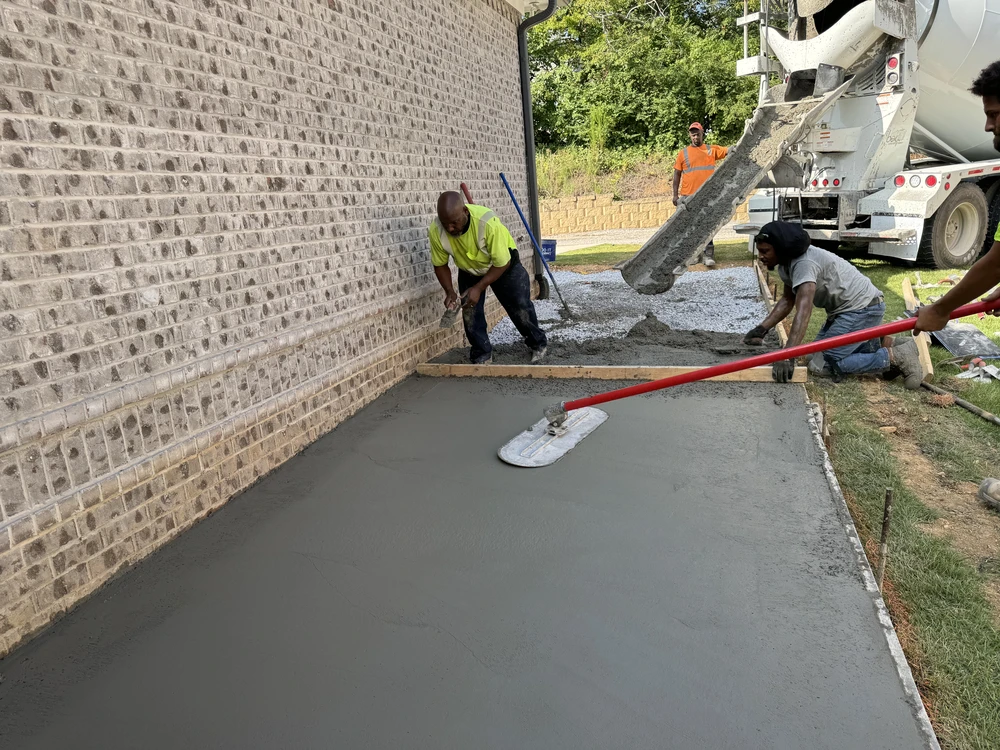 Workers smooth wet concrete patio beside a brick wall as a cement truck unloads at a Red Bank TN home.
