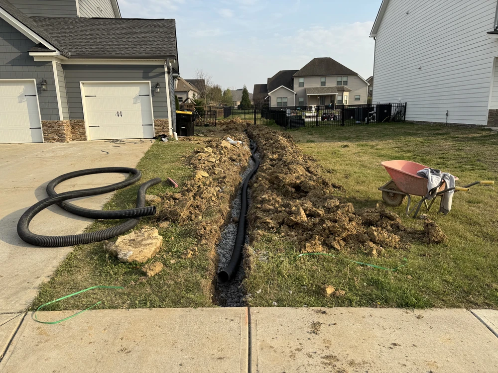 French drain trench with black corrugated pipe and wheelbarrow beside a garage on Lookout Mountain.